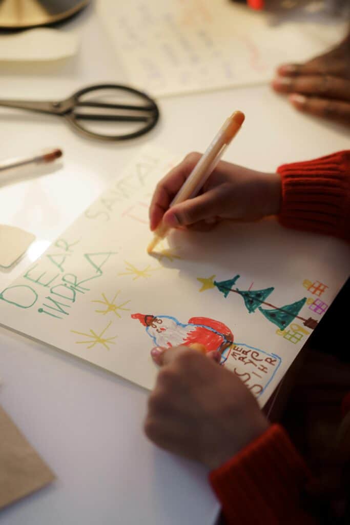 A child drawing a Christmas card, illustrating Santa and festive symbols.